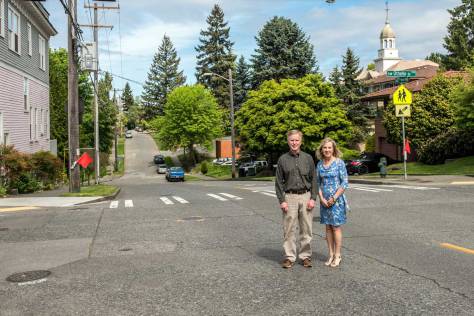 NOW: Descendants Stuart and Michele Kenney pose at the same intersection, sans trestle. The former Ashton Grocery building, shown in the “then” view, remains, at left. 